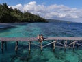 Couple sitting on a dock in a paradise beach in Raja Ampat, Indonesia