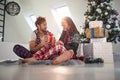 Young couple sitting on the floor in font of christmas tree beside pile of presents. female surprised by the gift from a boyfriend