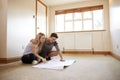 Couple Sitting On Floor Looking At Plans In Empty Room Of New Home Royalty Free Stock Photo