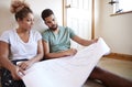 Couple Sitting On Floor Looking At Plans In Empty Room Of New Home Royalty Free Stock Photo