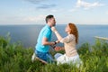 Couple sitting on grass face to face on knees in the grass on sea and sky background. Young couple enjoying outdoors rest.