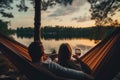 Couple sitting in hammock and drinking wine on the lake at sunset, person view couple resting at camping woman laying in hammock