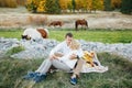 Couple is sitting hugging each other on a blanket with food on the lawn. Horses graze in the background Royalty Free Stock Photo