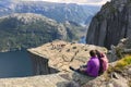 Couple sitting on a rock and admiring a view on Preikestolen. Aerial shot, upper perspective on the couple. Endless view of the fj