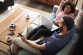 Couple Sitting On Sofa At Home Using Laptop Computer And Watching TV Royalty Free Stock Photo