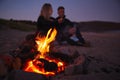 Couple Sitting On Surfboard By Camp Fire On Beach Using Mobile Phone As Sun Sets Behind Them Royalty Free Stock Photo