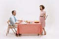 Portrait of couple sitting at the table, having breakfast isolated on white background. Movie remake. Wife hiding knife