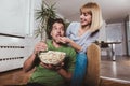 Couple sitting together on a sofa at home watching television, joyfully smiling eating pop corn enjoying a night in together Royalty Free Stock Photo