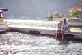 Couple sitting on wooden jetty by sea, having drink and flirting. Boats city and mountains in the background. Love, holiday, Royalty Free Stock Photo