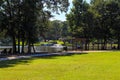 A couple sitting a wooden swing on the banks of the lake with a water fountain in the middle of the lake, lush green grass