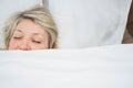 Mature woman lying under white duvet in bedroom with bed frame, white sheets and pillow Royalty Free Stock Photo