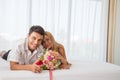 Couple smiling and lying in bed and holding flowers after the man had asked for marriage