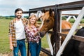 couple of smiling ranchers palming horse in stable and looking Royalty Free Stock Photo