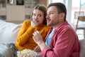 Emotional woman and intrigued man watching thriller, action film, scary movie at home eating popcorn