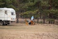 Couple starting a campfire to have dinner near their trailer on golden grass in autumn green pine tree forest Royalty Free Stock Photo