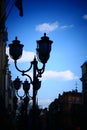 A couple of street lamps against a bright sky with lonely clouds.