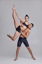 The couple of a young modern ballet dancers in black suits are posing over a gray studio background.