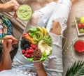 Couple in summer clothes holding fresh salad with quinoa, peach, greens, avocado, berries, melon in bowl on light background with Royalty Free Stock Photo