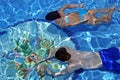 Couple swimming underwater in clear blue pool