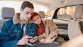 A couple of teenagers looking tired, using their smartphones while sitting together on back seat in the car Royalty Free Stock Photo