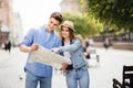 Young Couple of tourists is exploring new city together. Smiling and look at the map on the city street Royalty Free Stock Photo