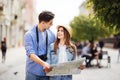 Young Couple of tourists is exploring new city together. Smiling and look at the map on the city street Royalty Free Stock Photo