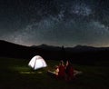 Couple tourists near campfire and tents under night sky full of stars and milky way Royalty Free Stock Photo