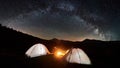 Couple tourists near campfire and tents under night sky full of stars and milky way Royalty Free Stock Photo