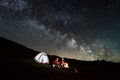 Couple tourists near campfire and tents under night sky full of stars and milky way Royalty Free Stock Photo