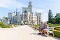 A couple of tourists are sitting on a bench in front of the beautiful castle Hluboka nad Vltavou - Czech Republic Royalty Free Stock Photo