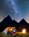 Couple tourists sitting near tent and campfire, looking to the shines starry sky and Milky way in the camping at night Royalty Free Stock Photo