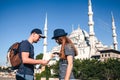 A couple of tourists a young man and a pretty woman look at the map next to the world-famous Blue Mosque also called Royalty Free Stock Photo