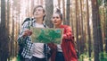 Couple of tourists young woman and man are studying map and looking around standing in forest on summer day wearing Royalty Free Stock Photo