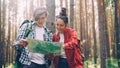 Couple of tourists young woman and man are studying map and looking around standing in forest on summer day wearing Royalty Free Stock Photo