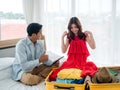 Couple travelers packing trip. Young Asian woman trying on clothes, red dress and man holding tablet for travel information. Royalty Free Stock Photo