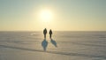 The couple of travelers walking through the snow field on sunset background. Royalty Free Stock Photo