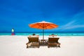 Couple on a tropical beach on deck chairs under a red umbrella.