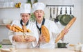 Couple two Asian professional chefs wearing white uniform, hat, showing, holding baguette, bread, cooking breakfast in kitchen Royalty Free Stock Photo