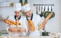 Couple two Asian professional chefs wearing white uniform, hat, showing, holding baguette, bread, cooking breakfast in kitchen Royalty Free Stock Photo