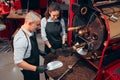 Couple of two baristas checking the quality of the coffee beans standing with scoop near the roaster machine at the roastery. High Royalty Free Stock Photo