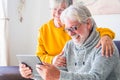 Couple of two cheerful and happy mature and old people seniors using tablet and having fun sitting on the sofa at home together. Royalty Free Stock Photo
