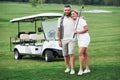 Couple of two golfers staying on the green lawn with cart behind of them Royalty Free Stock Photo