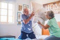 Couple of two happy seniors having fun playing together on the bed at home fighting with pillows enjoying - pillows war indoors in Royalty Free Stock Photo