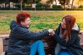 Couple of two lesbian women, smiling, sitting, holding hands on a bench in a public park. Royalty Free Stock Photo