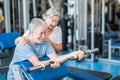 Couple of two seniors at the gym doing exercise together having fun to be healthy and fit - man holding a barr without weight and Royalty Free Stock Photo