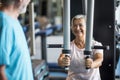 Couple of two seniors at the gym training together - woman doing a exercise in a machine and the mature man is looking at her - Royalty Free Stock Photo