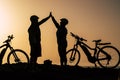 Couple of two seniors and mature people together at the sunset with their bikes giving five with the silhouette and the sea at the Royalty Free Stock Photo