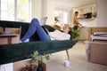 Couple Unpacking Boxes After Moving Into New Home Together As Woman Lies On Sofa Using Laptop Royalty Free Stock Photo