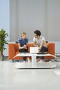 Couple Using Laptop On Orange Sofa At Office