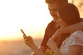 Couple using a smartphone in a sunset back light Royalty Free Stock Photo